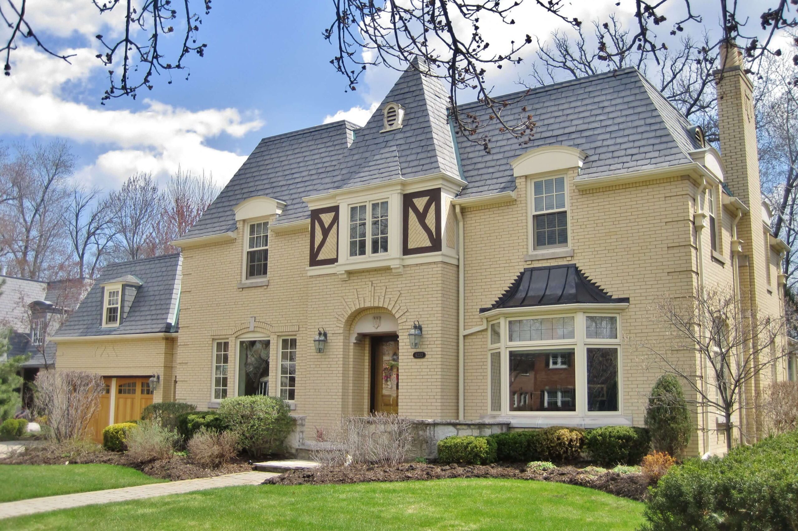 A large yellow brick french colonial house with a gray roof