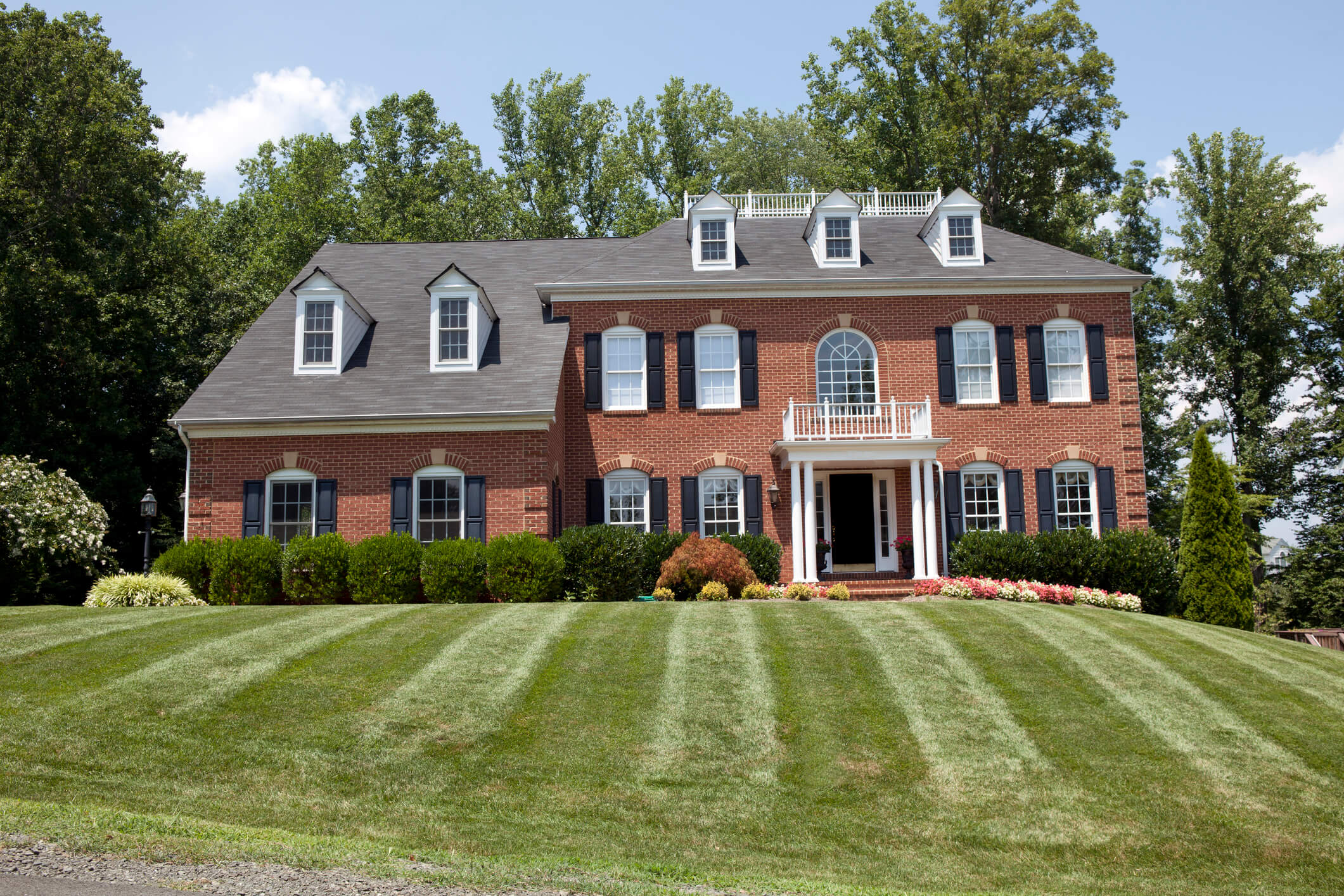 A large red brick french colonial house with a lawn in front of it 