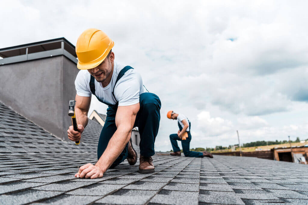 Two men working on a roof with a hammer
