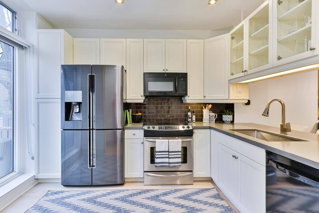 A kitchen with white cabinets and refrigerator, oven, microwave and other steel appliances
