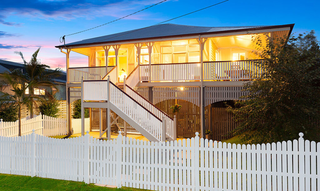 Queenslander homes with a white picket fence in front of it 