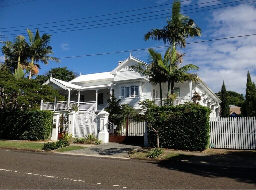 queenslander style home with palm trees and a white fence 
