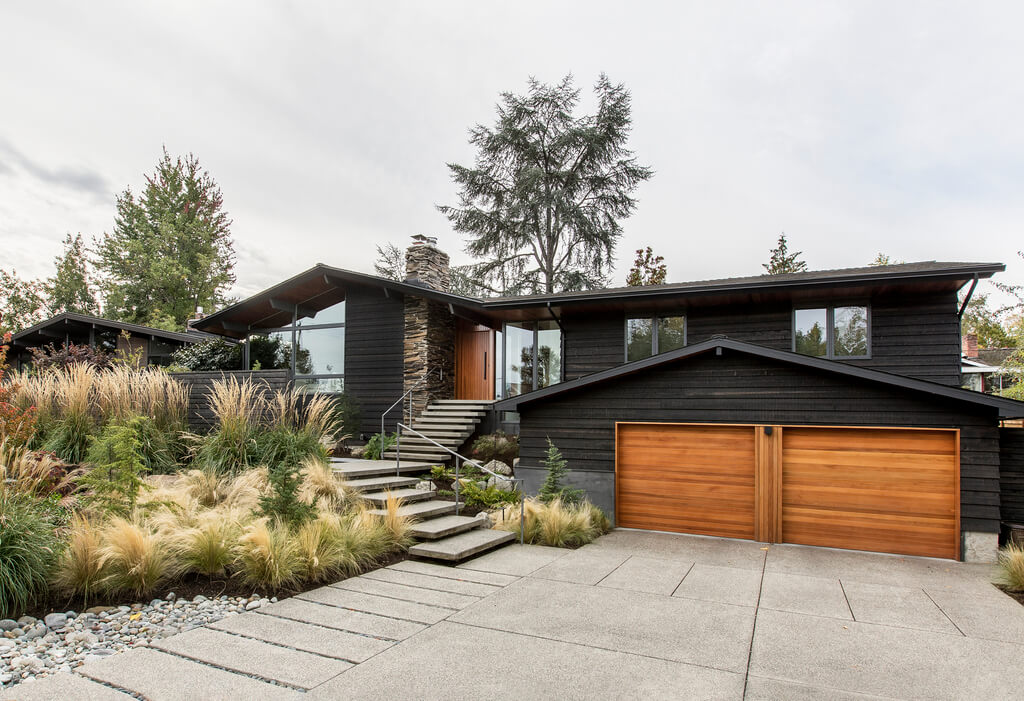 XA black ranch house with a wooden garage door 