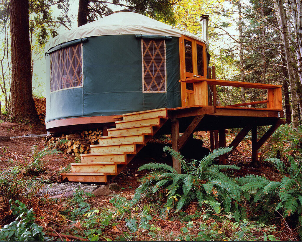 A yurt in the woods with stairs leading up to it
