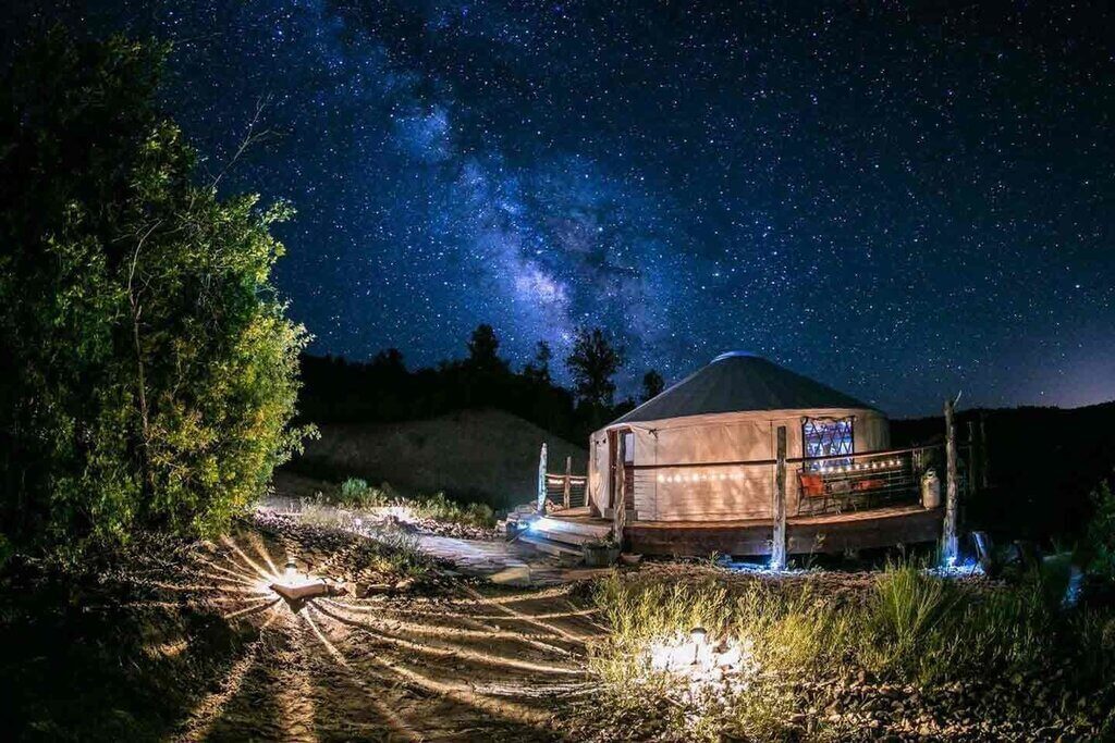 A yurt in the middle of a field under a night sky filled with stars
