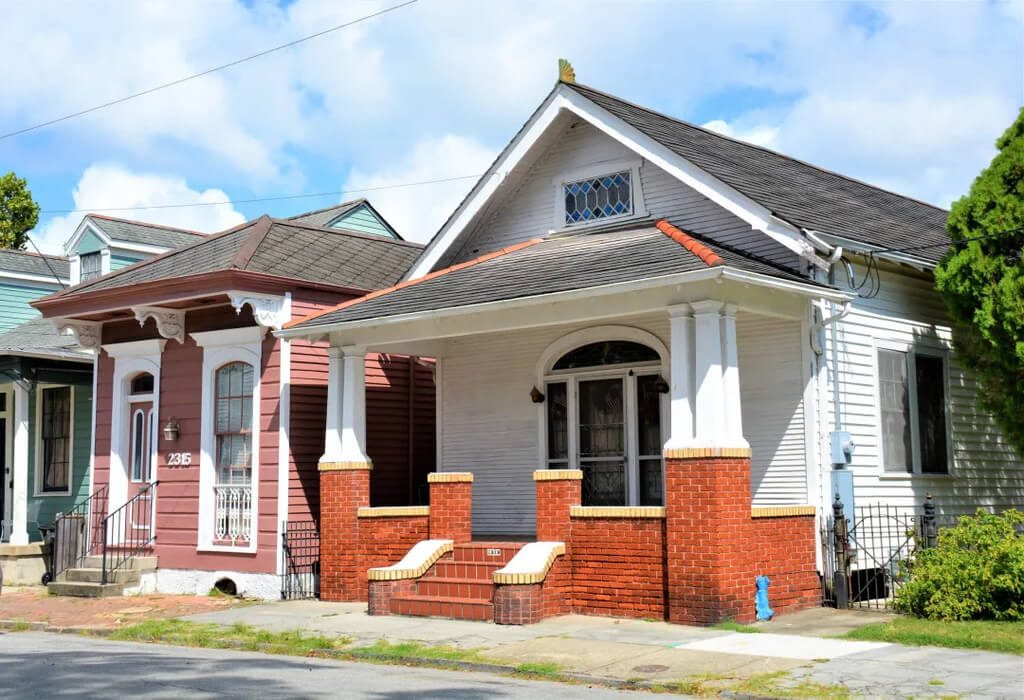 A small white shotgun style houses with red brick and white trim
